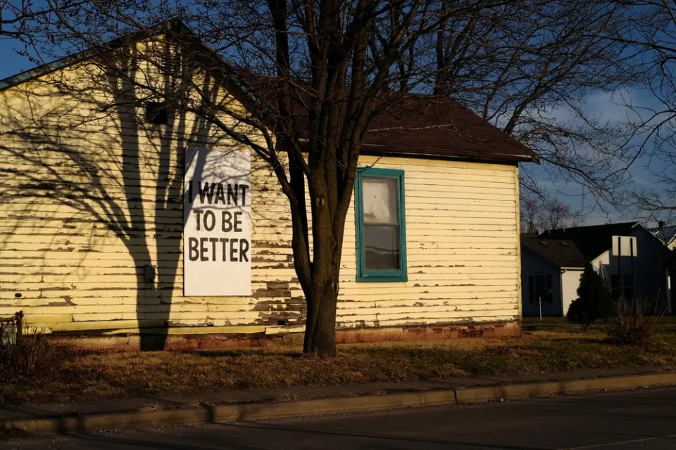 Single-story wooden home with weathered paint and "I want to be better" sign